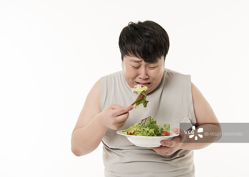演播室照片：节食中的男子吃沙拉，神情悲伤图片素材