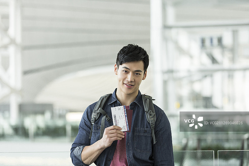 青年男子背着包展示机票和护照在机场图片素材