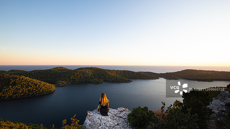 日落时分，坐在石头上俯瞰大海的女人图片素材