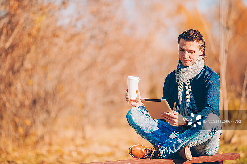 坐在长椅上使用平板电脑的年轻人图片素材