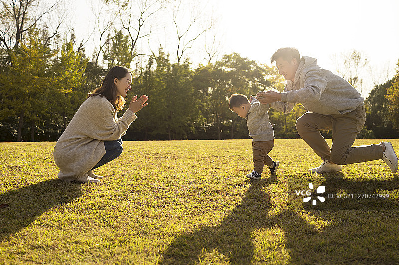 年轻夫妇在草地上教宝宝走路图片素材