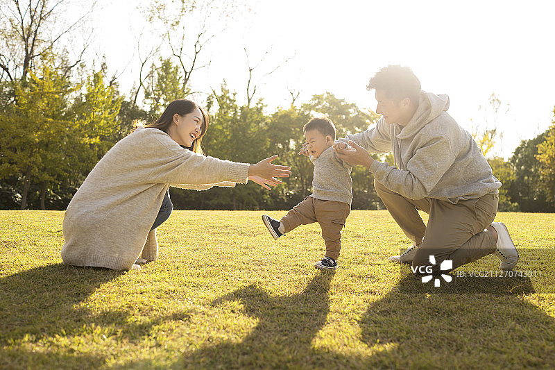 年轻夫妇在草地上教宝宝走路图片素材