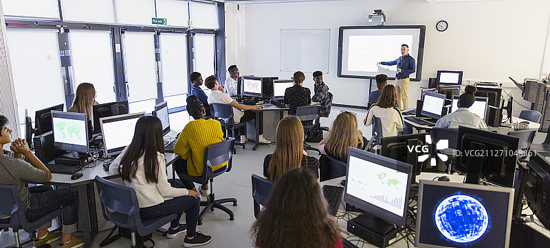 初中生在教室里使用电脑并观看投影屏幕上的老师图片素材