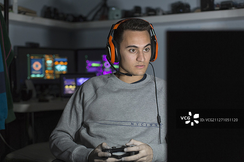 戴着耳机的专注少年在黑暗房间里用电脑玩电子游戏图片素材