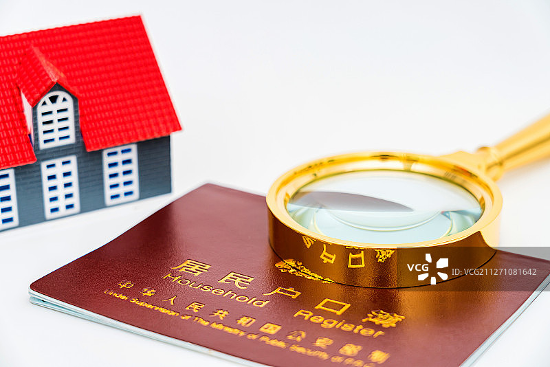 放大镜和房子模型放在居民户口本上图片素材