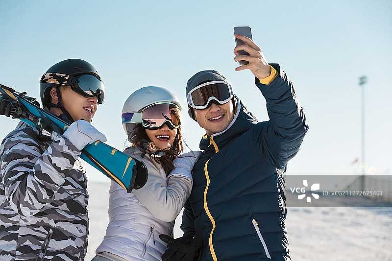 三个青年男女在户外滑雪场拿手机拍照合影图片素材