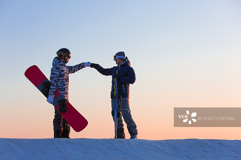 日落下两个年轻男子在滑雪场顶拳问候图片素材