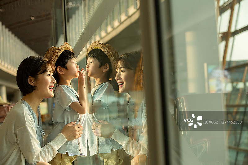 年轻妈妈和儿子从机场候机厅往外看图片素材