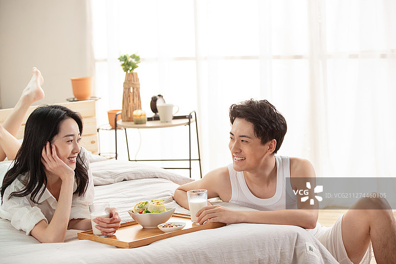 快乐的年轻情侣在床上吃早餐图片素材