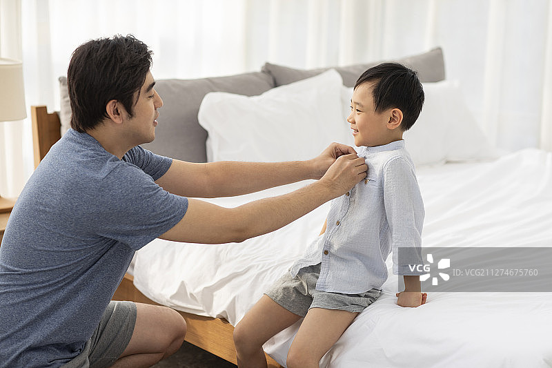 父亲在卧室帮助儿子穿衣服图片素材