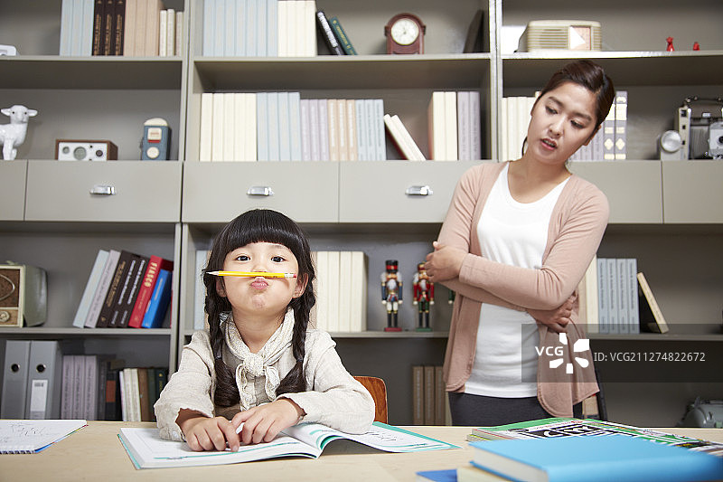 母亲看着坐在桌旁学习的女儿图片素材
