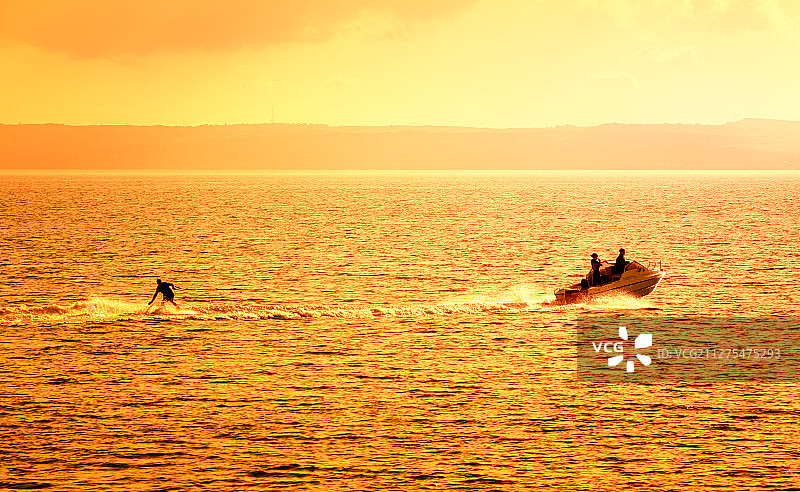 夏天日落金色海面上摩托艇和滑水运动员剪影图片素材