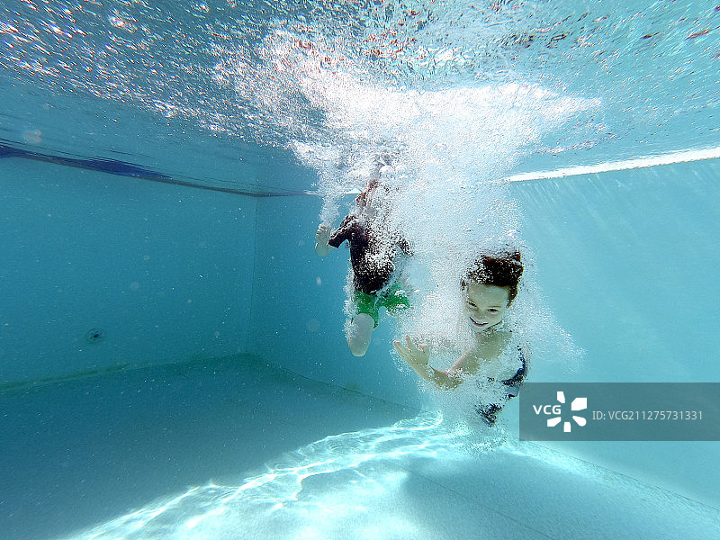 孩子们在清澈的蓝色游泳池中水下游泳图片素材