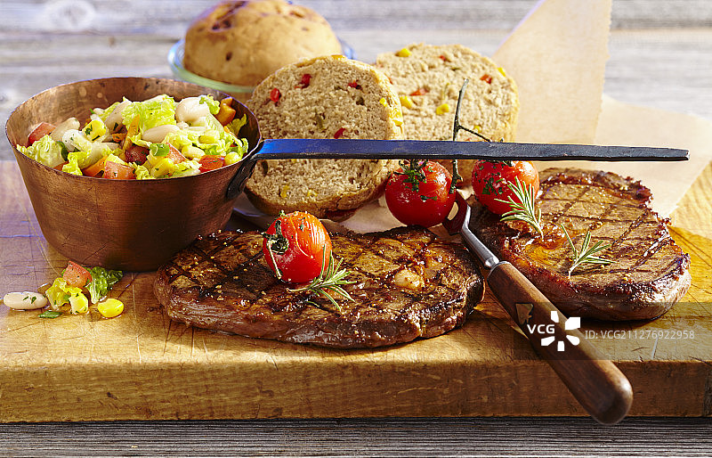 搭配蔬菜沙拉和面包、小番茄、迷迭香和复古铜罐的烤牛排图片素材