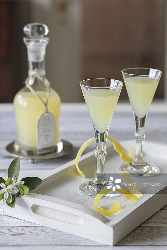 玻璃瓶装柠檬酒和木制托盘上的两个玻璃杯图片素材