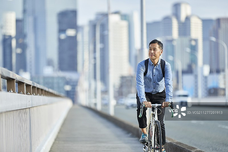 在日本大阪市中心骑自行车的成熟日本男人图片素材