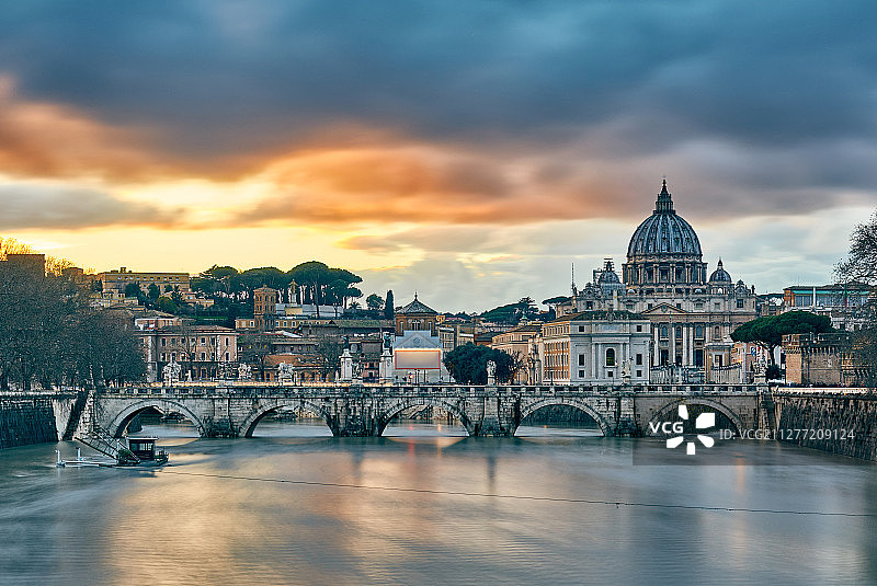 傍晚时分，水势高涨的台伯河畔的圣彼得大教堂与戏剧性的日落天空。意大利罗马梵蒂冈圣彼得大教堂与圣天使桥图片素材