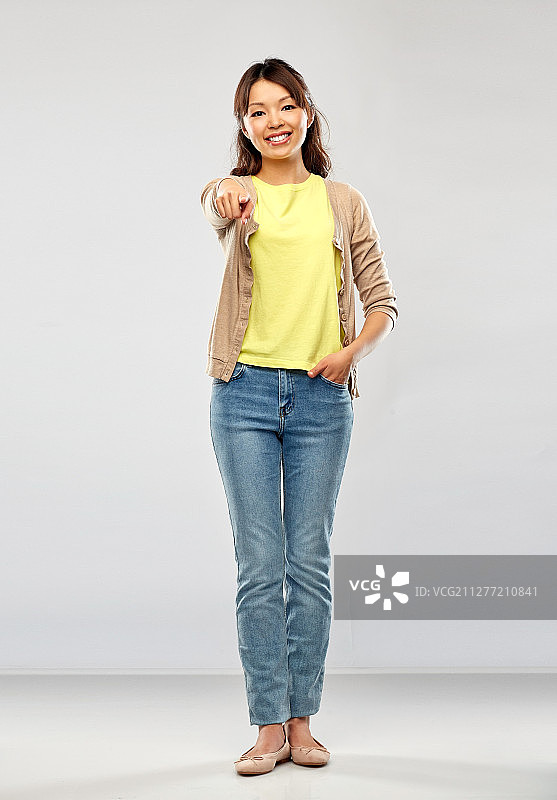 人物肖像：快乐的亚洲年轻女人在灰色背景前指向你图片素材