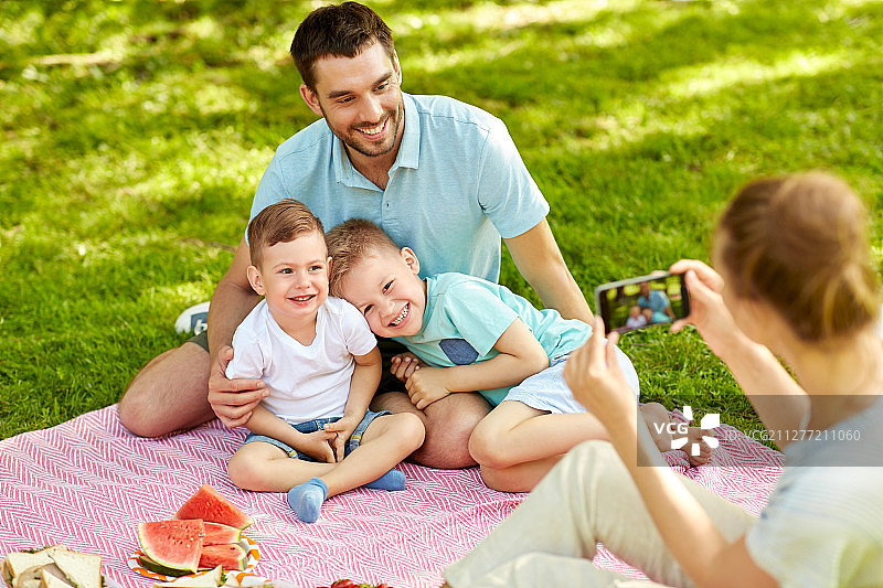 母亲用手机拍摄在公园野餐的幸福家庭图片素材