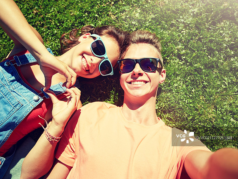 爱与人概念 - 快乐的青少年情侣戴着太阳镜躺在草地上自拍图片素材