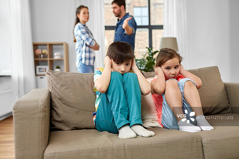 家庭问题，冲突和人际关系概念-悲伤的孩子捂住耳朵，而父母在家中争吵。悲伤的孩子和父母在家中争吵图片素材