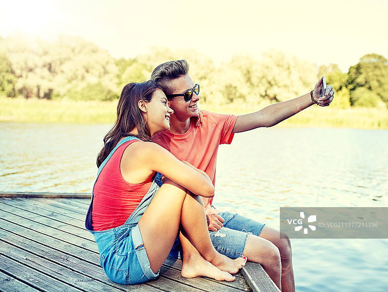 假日情侣：在河边用智能手机自拍的青少年图片素材
