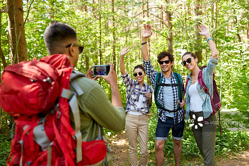 旅行、旅游和徒步概念——朋友们在森林中用智能手机拍照图片素材