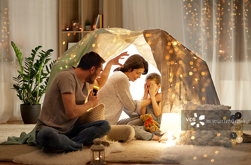 舒适和家庭概念 - 父亲用手电筒在儿童帐篷里给女儿和妻子讲恐怖故事图片素材