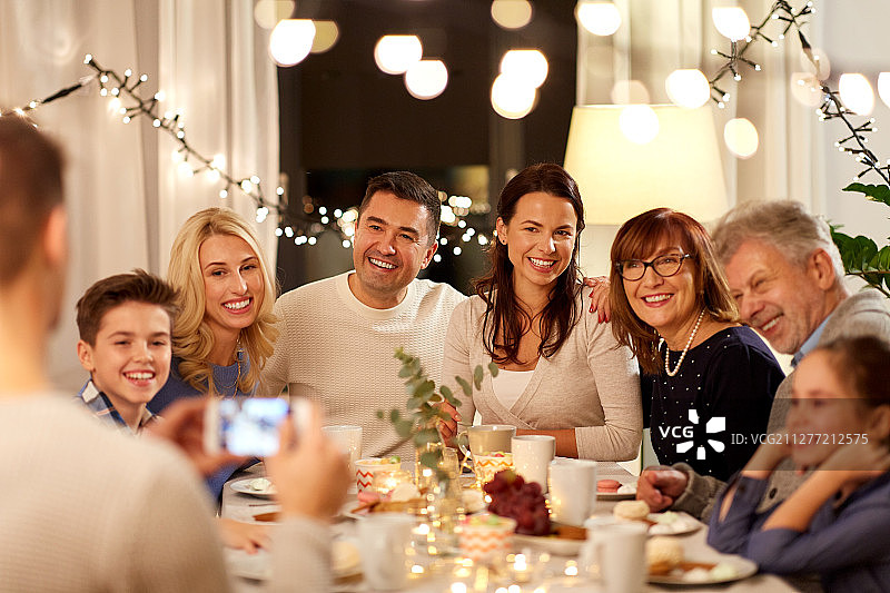 庆祝节日：快乐的家庭在家中用智能手机举办茶话会并拍照图片素材