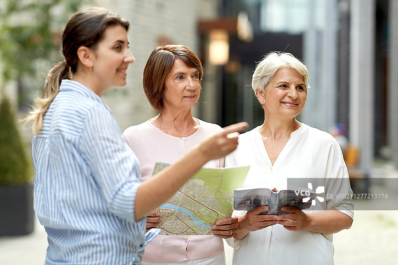 旅游，旅行和友谊的概念-女性路人显示方向的妇女与城市指南和地图塔林街。路人向城市里的老年妇女指路图片素材