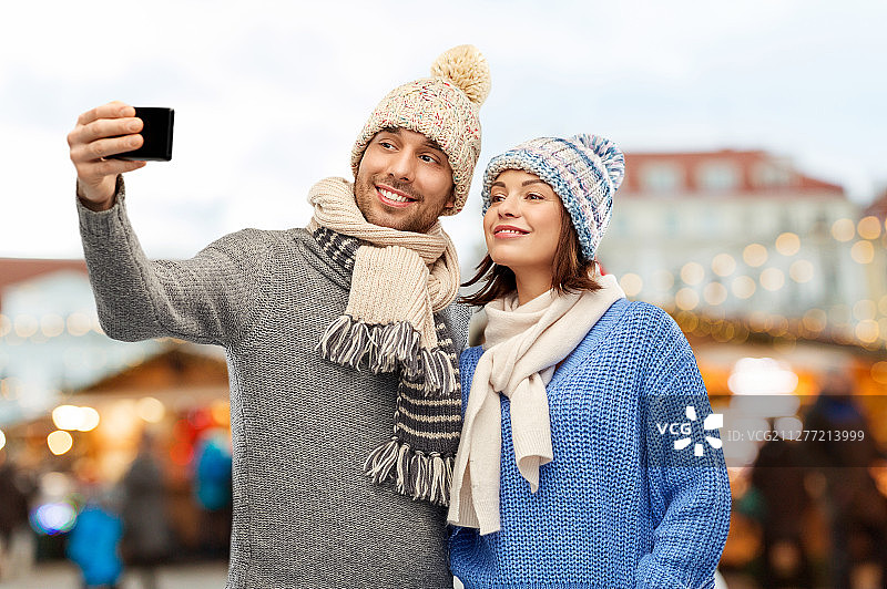 在塔林老城的圣诞市场，一对戴着针织帽和围巾的幸福情侣用智能手机自拍图片素材