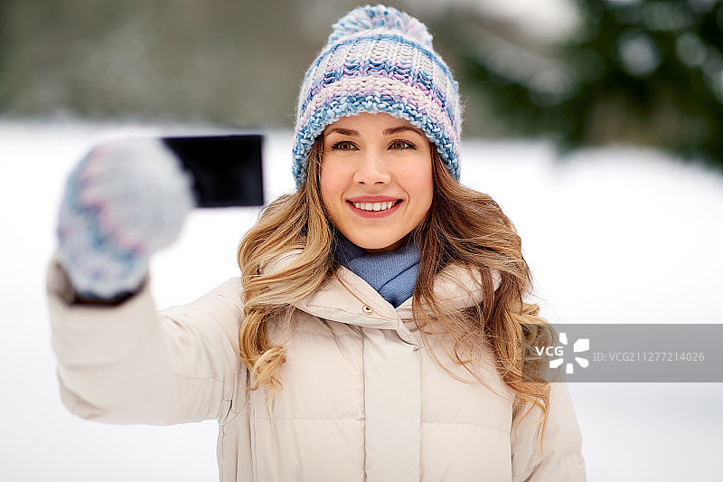 冬天用智能手机自拍的快乐微笑的女人图片素材