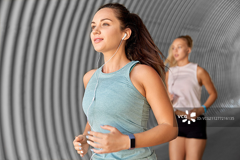 健身、运动与健康生活方式理念：戴着耳机在户外跑步的年轻女性朋友图片素材