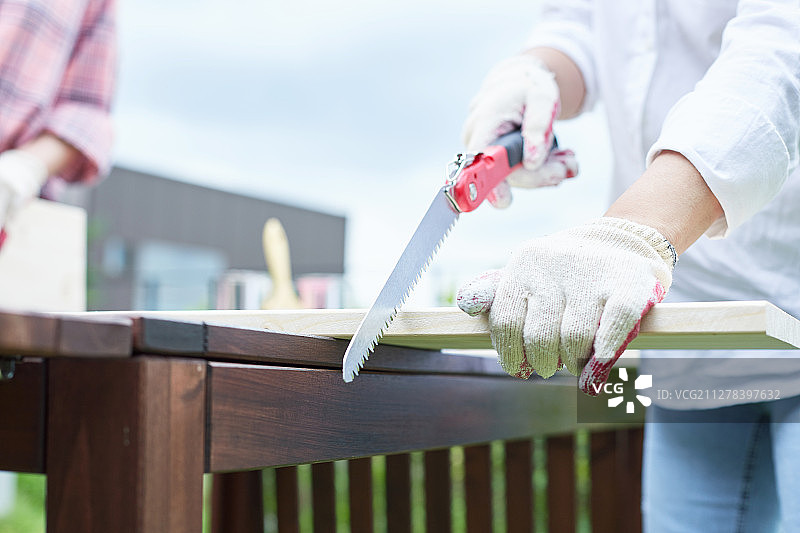 中年妇女的爱好：微笑，锯木头，戴工作手套图片素材