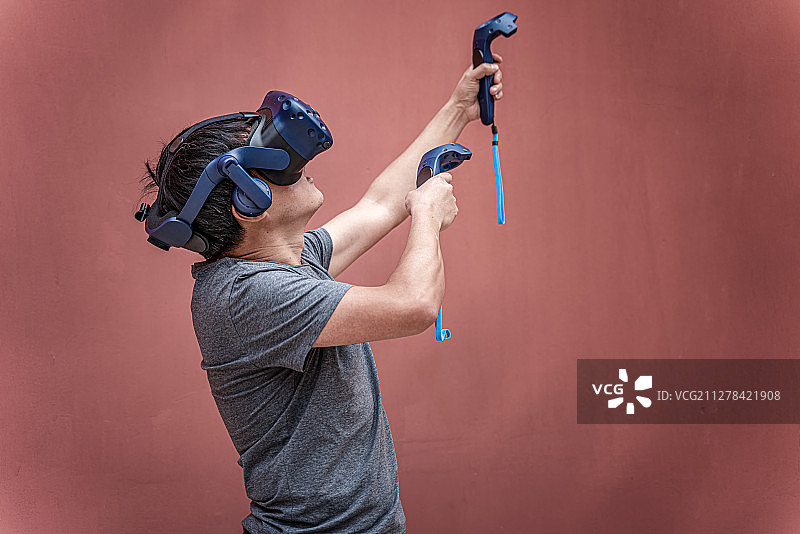 一个中国男人戴着VR虚拟现实眼镜拿着游戏手柄体验图片素材