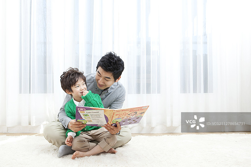 父亲在客厅里坐在地上给儿子读书的摄影图片素材
