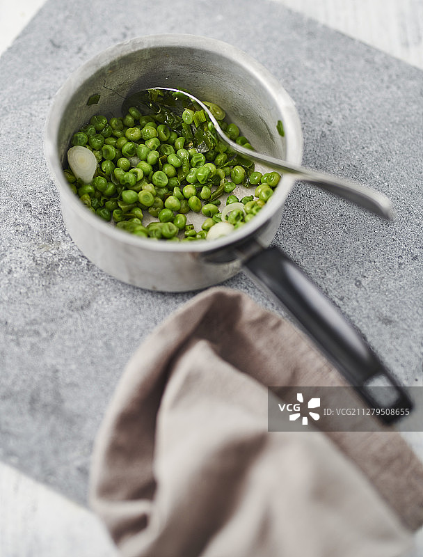 在灰色的工作台上，用勺子和一块布把豌豆放在平底锅里图片素材