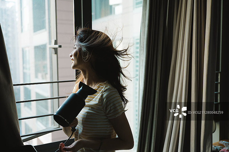 亚洲年轻女孩用吹风机吹头发图片素材