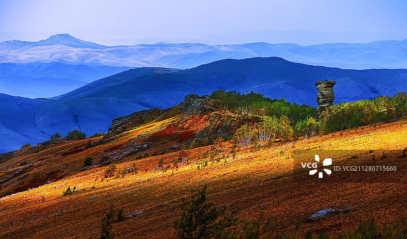 山峦层叠，秋林中矗立着一尊花岗岩石柱。图片素材