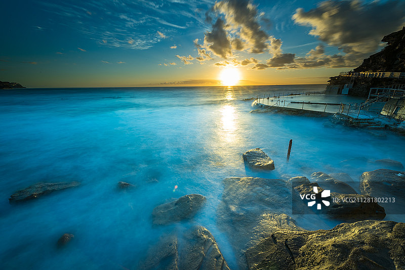 日出时分的悉尼海滩，海浪拍打岩石，激起朵朵浪花图片素材