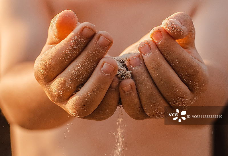 夕阳阳光下，儿童的手释放出流过手中的沙子图片素材