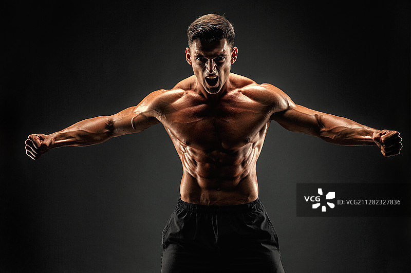 在深色背景下怒吼以激励的健壮男人图片素材