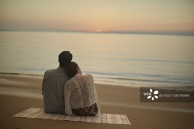 情侣坐在垫子上，在海滩上看日落摄影图片素材