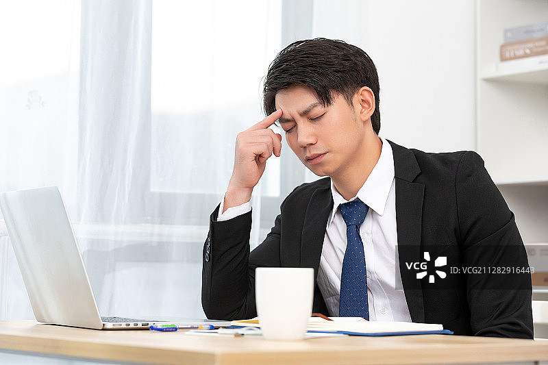 坐在桌子旁边头疼的亚洲商务男士， 金融商业保险图片素材