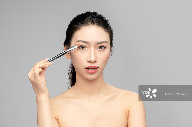 灰色背景里正在使用眉笔的亚洲美女面部特写，化妆护肤整容图片素材