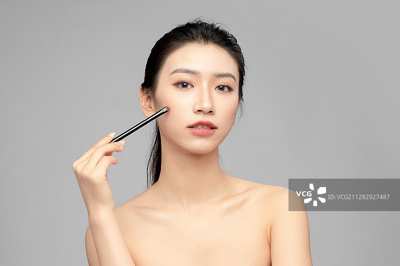 灰色背景里正在使用眉笔的亚洲美女面部特写，化妆护肤整容图片素材