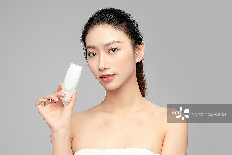 灰色背景里手中拿着洗面奶瓶子作为展示的亚洲美女面部特写，化图片素材