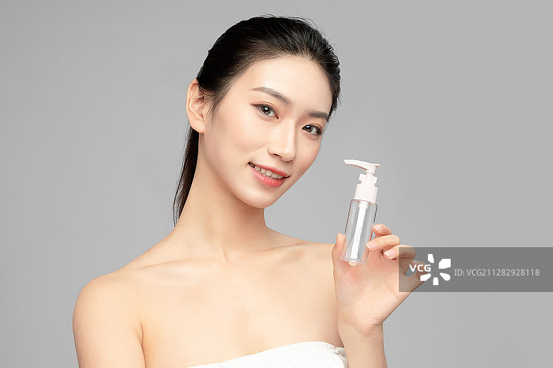 灰色背景里手中拿着洗面奶瓶子作为展示的亚洲美女面部特写，化图片素材