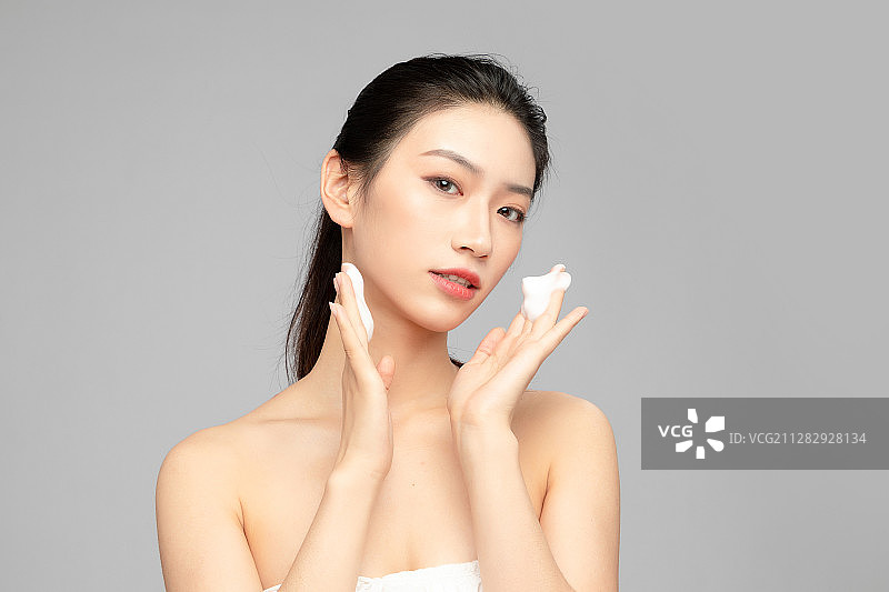 灰色背景里正在使用洗面奶的亚洲美女面部特写，化妆护肤整容图片素材