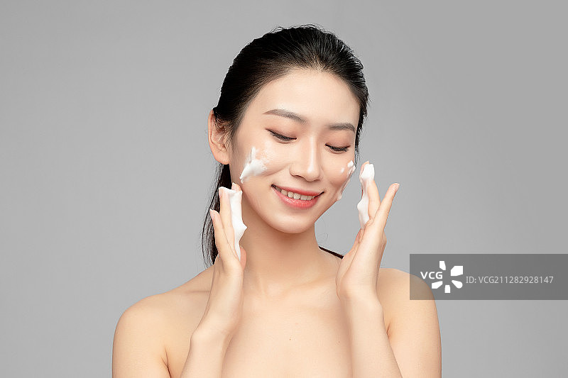 灰色背景里正在使用洗面奶的亚洲美女面部特写，化妆护肤整容图片素材